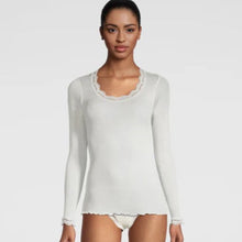 Load image into Gallery viewer, A woman modeling a white long-sleeve ribbed silk knit top with calais lace neckline, shown against a plain light gray studio background.