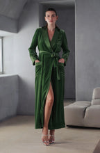 Load image into Gallery viewer, A woman wearing an Ivy green silk velvet full length dressing gown. It is tied at the waist with a belt that has a satin side. The pockets are at the front with a satin trim including a statement breast pocket. The lapel and cuffs also are finished in satin silk.