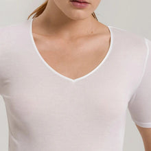 Load image into Gallery viewer, A woman wearing a white seamless cotton T-Shirt style top. It has a short sleeves and a V-Neck. This image showcases the finishes of the sleeve and the satin trim on the V-Neck.
