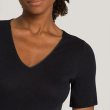 Load image into Gallery viewer, A woman wearing a black seamless cotton T-Shirt style top. It has a short sleeves and a V-Neck. This image showcases the finishes of the sleeve and the satin trim on the V-Neck.