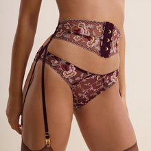 Load image into Gallery viewer, A close-up of a model wearing a sheer floral embroidery lingerie set with a garter belt and attached garter straps with gold-tone hardware, against a solid light beige background.