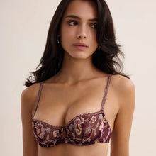 Load image into Gallery viewer, A woman modeling a sheer floral underwire bra in deep burgundy with gold embroidery, set against a solid light beige background.