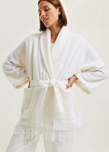 Load image into Gallery viewer, SALE Playful poncho style short wool robe. It has a wide shawl collar with fringe detail at the hem. Belted at the waist and with a large patch pocket to the front, this garment may be worn as lingerie or outerwear. Wherever it guarantees cosiness!
Fabric Content: 80% Wool, 20% Polyamide
95cm in length. Ivory.