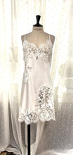 Load image into Gallery viewer, Made in Florence, this is a beautiful pure silk satin slip or nightgown. There is stunning deep appliqué lace on the bust. A side wide lace split leads from the thigh to the hem, continuing all around the base of the garment. There are French seams throughout for softness. The fine spaghetti straps are adjustable for the perfect fit. This nightslip is cut on the bias and panelled, giving a lovely flare and movement. May be worn as underwear, nightwear or outerwear. Ivory.