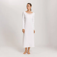 Load image into Gallery viewer, A woman wearing an Off White long sleeve full length (130cm) nightdress. It has a lovely round neckline embellished with a delicate embroidered lace trim on tulle. The garment has a lovely feminine flow to it with a slit on the side to allow for comfortable movement.