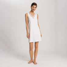 Load image into Gallery viewer, A woman wearing an Off White sleeveless short (knee length) nightdress. The deep V-neck is adorned with a wide embroidered lace trim on tulle. The garment has a lovely feminine flow to it.