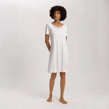 Load image into Gallery viewer, A woman wearing an Off White short (knee length) nightdress with short sleeves and a lace trim on the neckline. The garment has a lovely feminine flow to it.