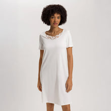 Load image into Gallery viewer, A woman wearing an Off White short (knee length) nightdress with short sleeves and a lace trim on the neckline. The garment has a lovely feminine flow to it.