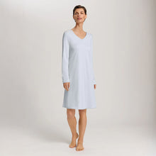 Load image into Gallery viewer, A woman wearing a powder blue long sleeve cotton silk knee length nightdress. It has a silk trim on the V-neck as well as on the sleeves and the hem