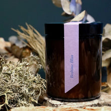 Load image into Gallery viewer, Candle labeled 'Bedtime Bliss' with a purple tag, surrounded by natural elements.