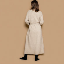Load image into Gallery viewer, A woman viewed from behind wearing a long, light beige cashmere knitted coat with a matching belt, paired with black socks, against a solid beige background.