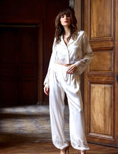 Load image into Gallery viewer, Wonderfully playful Harem style silk satin pyjamas. The button front Crop Top has a revere collar, the jacket hem has a wide appliqué lace detail, mirrored in the deep appliqué lace on the cuffs. The trousers has an elastic waist band at the back, and flat to the front. The bottom of the pants has a wide appliqué lace band, tapering into a cuff at the ankle. French seams throughout. Perfect for sleep or leisure wear.
Fabric: 50% Silk, 38% Viscose, 12% Spandex
Lace: 100% Polyester.
