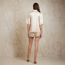 Load image into Gallery viewer, Image of the back. Short sleeve shortie pyjamas in champagne with contrast seam in black colour. The top is hip length, and the sleeve at elbow length has contrast piping on the trim. Shots end just above mid thigh with a matching contrast trim on the bottom.