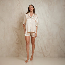 Load image into Gallery viewer, Short sleeve shortie pyjamas in champagne with contrast seam in black colour. The top is hip length, and the sleeve at elbow length has contrast piping on the trim. Buttons down the front. Shots end just above mid thigh with a matching contrast trim on the bottom. Notched collar features the contrast piping which follows the edge all the way down the centre opening.
