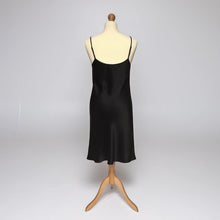 Load image into Gallery viewer, A black silk satin slip displayed on a cream mannequin torso with a wooden tripod stand against a light gray studio background.