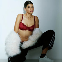 Load image into Gallery viewer, Woman wearing a red bra and black pants with white fur, sitting on a light gray background.
