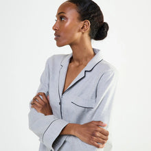 Load image into Gallery viewer, A woman wearing a light gray long-sleeve pajama shirt with black piping trim, posed against a clean white background.
