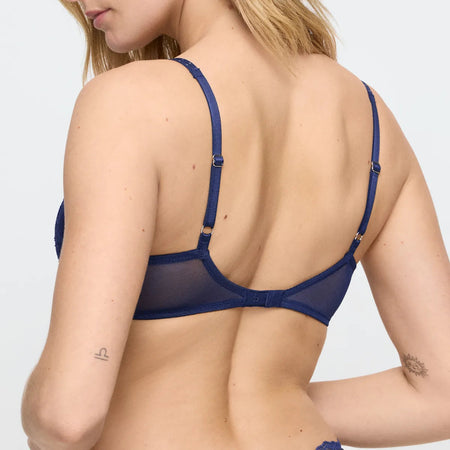 Nude woman wearing a blue bra against a white background