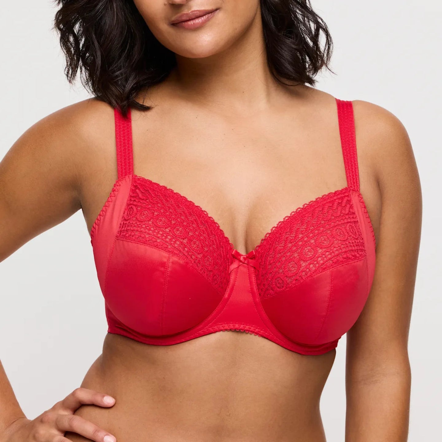 Red bra with lace details worn by a model on a plain background