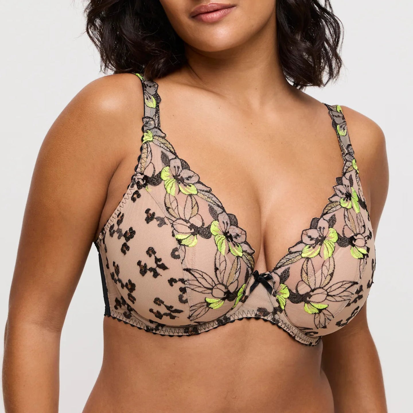 Woman wearing a floral lace bralette with green accents on a plain background