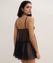 Load image into Gallery viewer, A woman wearing a sheer black mesh babydoll lingerie chemise, photographed from the back against a plain light beige studio background.
