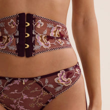 Load image into Gallery viewer, Close-up of a model wearing sheer burgundy mesh lingerie with pink, gold, and green floral embroidery, featuring a matching waistband with gold-tone hardware.
