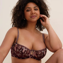 Load image into Gallery viewer, A woman with curly dark hair wearing a brown floral embroidered underwire bra with patterned straps, posed against a solid beige background.
