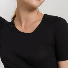 Load image into Gallery viewer, A woman wearing a black seamless cotton T-Shirt style top. It has a short sleeves and a V-Neck. This image showcases the finishes of the sleeve and the satin trim on the neckline. 
