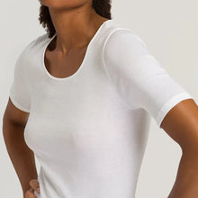 Load image into Gallery viewer, A woman wearing a white seamless cotton T-Shirt style top. It has a short sleeves and a V-Neck. This image showcases the finishes of the sleeve and the satin trim on the neckline. 
