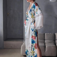 Beryl Full length robe. 
A fabulous floral pattern with an embroidered rendering. Entirely made of mixed silk satin, with a floral print on an ivory background, it seduces with its fluid and majestic look.
The pattern, both poetic and bright, evokes the refinement of watercolor embroidery, in a palette of deep and vibrant shades.
The cut is straight, loose, crossed at the front. The waist is accentuated by a matching belt with decorative long fringe. The wide sleeves, also enhanced with silky fringe.