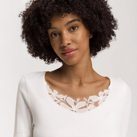 A close up of a woman wearing an Off White nightdress with short sleeves highlighting a lace trim on the neckline.