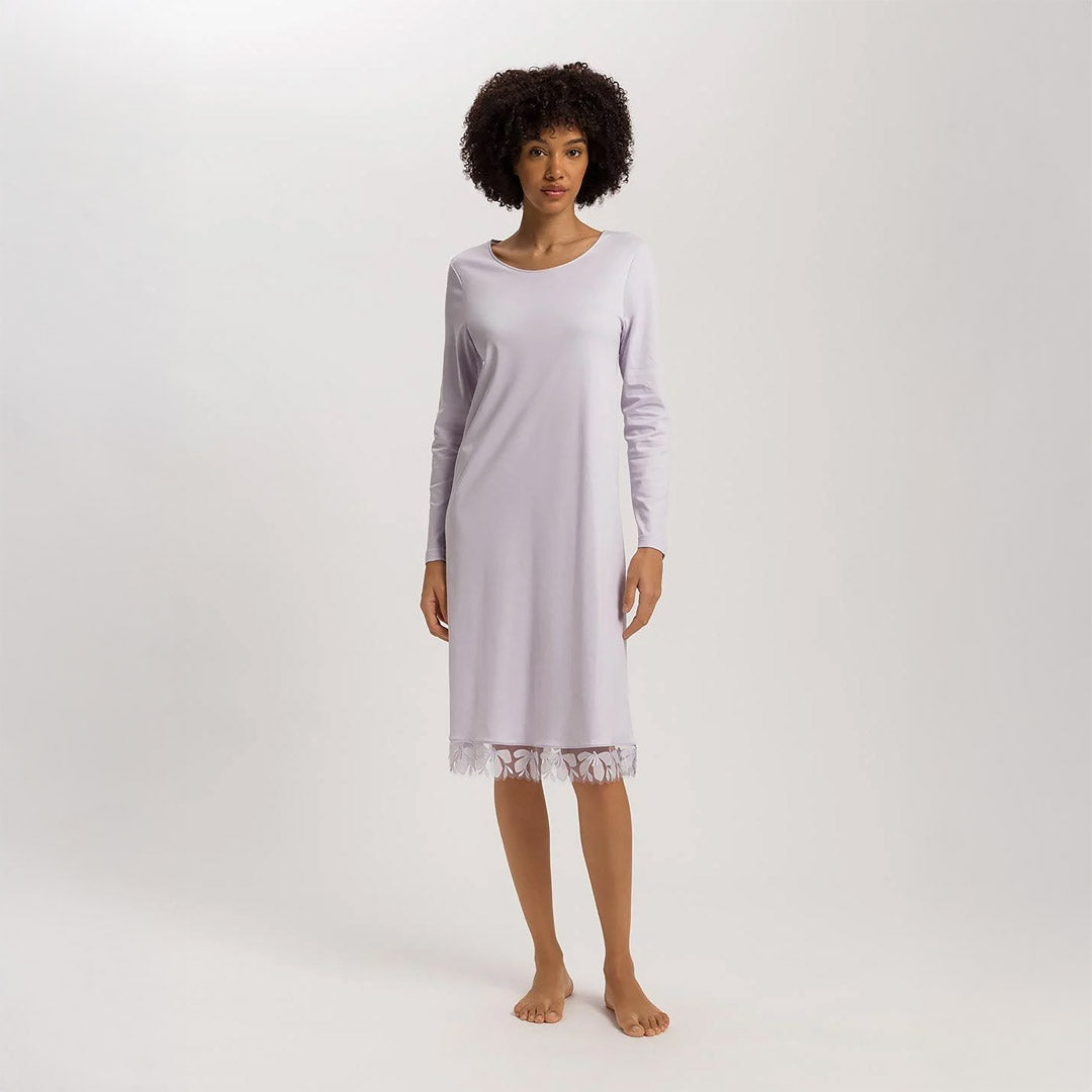 A woman wearing a Pink Lavender long sleeve 110cm length nightdress. It has a lovely round neckline and the hem has delicate embroidered lace trim on tulle.The garment has a lovely feminine flow to it.