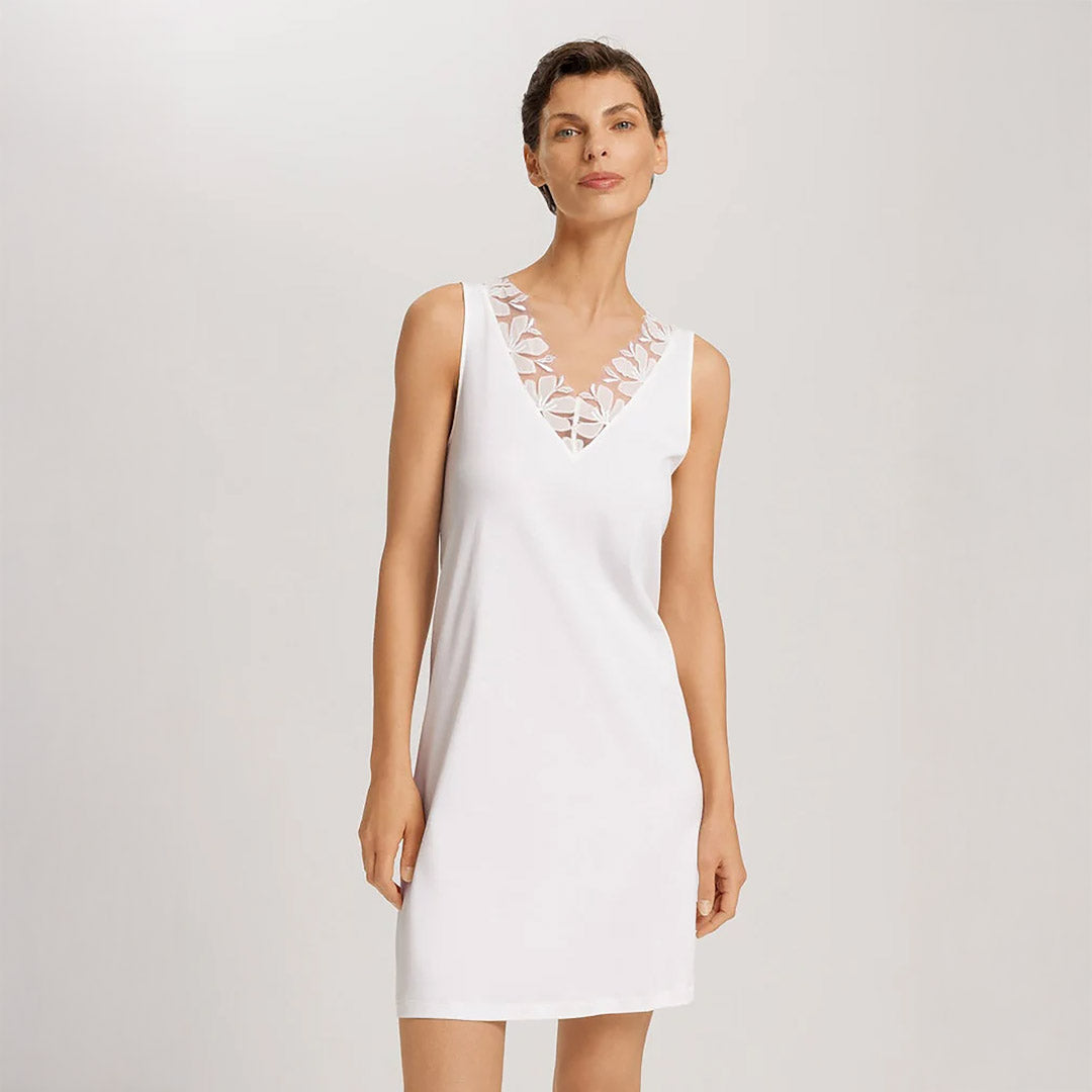 A woman wearing an Off White sleeveless short (knee length) nightdress. The deep V-neck is adorned with a wide embroidered lace trim on tulle. The garment has a lovely feminine flow to it.