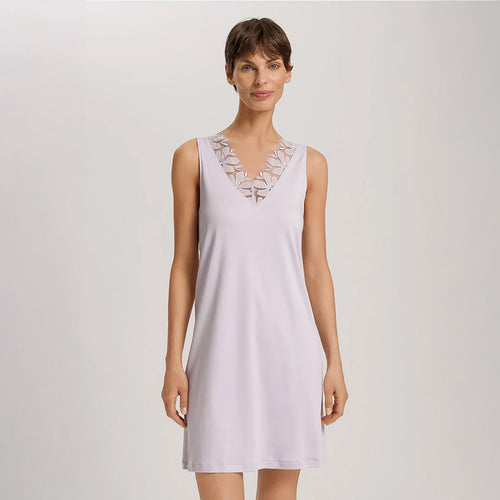 A woman wearing a Pink Lavender sleeveless short (knee length) nightdress. The deep V-neck is adorned with a wide embroidered lace trim on tulle. The garment has a lovely feminine flow to it.