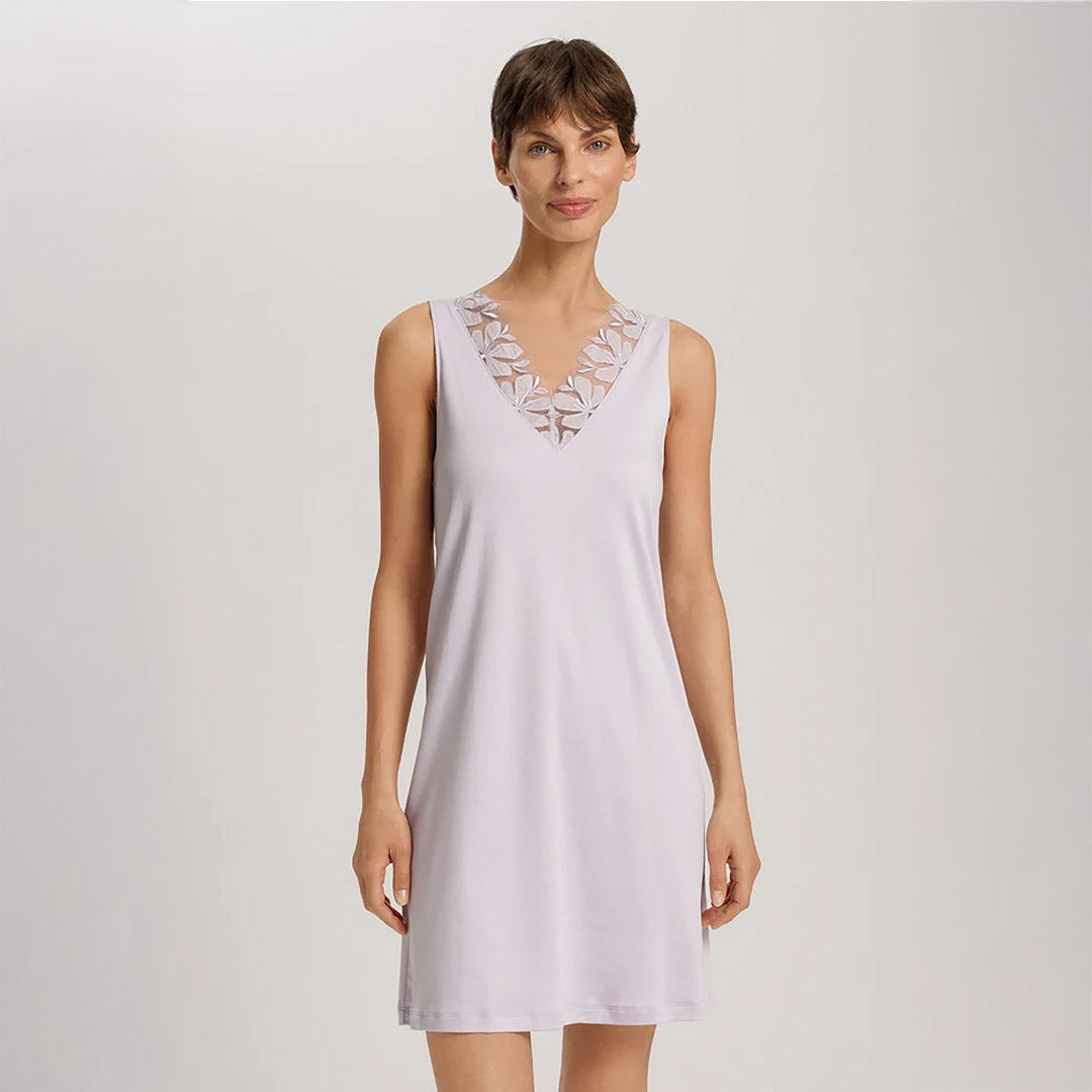 A woman wearing a Pink Lavender sleeveless short (knee length) nightdress. The deep V-neck is adorned with a wide embroidered lace trim on tulle. The garment has a lovely feminine flow to it.