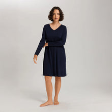 Load image into Gallery viewer, A woman wearing a navy long sleeve cotton silk knee length nightdress. It has a silk trim on the V-neck as well as on the sleeves and the hem. 
