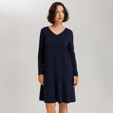 Load image into Gallery viewer, A woman wearing a navy long sleeve cotton silk knee length nightdress. It has a silk trim on the V-neck as well as on the sleeves and the hem. 
