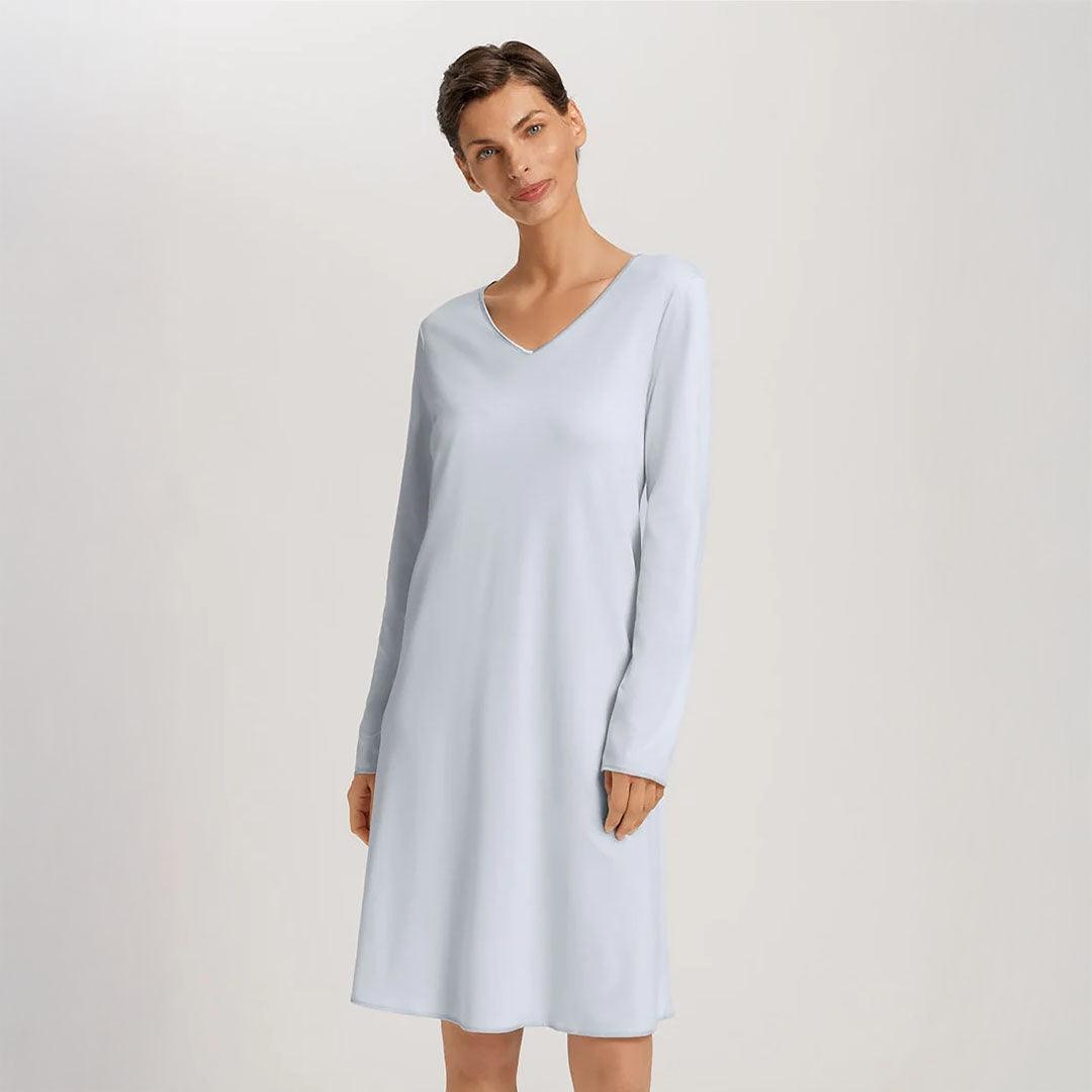 A woman wearing a powder blue long sleeve cotton silk knee length nightdress. It has a silk trim on the V-neck as well as on the sleeves and the hem