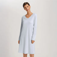 A woman wearing a powder blue long sleeve cotton silk knee length nightdress. It has a silk trim on the V-neck as well as on the sleeves and the hem