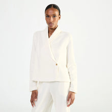 Load image into Gallery viewer, A model wearing a structured white wrap-style bed jacket with a single button closure, photographed against a clean white studio background.
