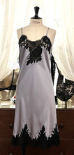 Load image into Gallery viewer, Silver/Black. Made in Italy, this is a beautiful long pure silk satin night/slip. There is stunning deep appliqué lace at the bust and hem. There are French seams throughout for softness. The fine spaghetti straps are adjustable for the perfect fit. This nightslip is cut on the bias and panelled giving lovely flare and movement. Perfect for bed or daywear. May be worn as underwear, nightwear or outerwear.   Composition: 100% Silk Satin Italian Lace 100% polyamide Machine washable Length 82cm from nape.
