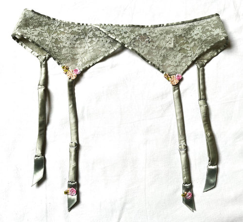 Very pretty Jade lace & silk suspender belt. It has four adjustable suspenders with a floral detail at the top and bottom of the front two. Three hook detail at the back.   Fabric Content: 81% Polyamide, 12% Silk, 7% Elastane.
