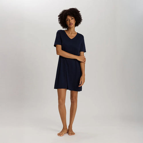 A woman wearing a navy short sleeve cotton silk above knee length 90 cm long nightdress. It has a silk trim on the V-neck as well as on the sleeves and the hem. 