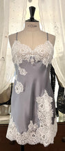 Load image into Gallery viewer, Made in Florence, Italy, this is a beautiful short pure silk satin night/slip. There is stunning deep appliqué lace on the bust and front of the garment. A side split leads to the hem, all with the same rich lace detail. There are French seams throughout for softness. The fine spaghetti straps are adjustable for the perfect fit. This nightslip is cut on the bias and panelled, giving lovely flare and movement. Perfect for bed or daywear. May be worn as underwear, nightwear or outerwear. Silver/Ivory.
