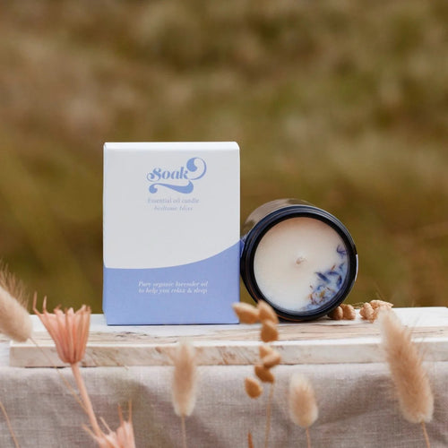 Candle and packaging with 'Soak' branding on a wooden surface with dried plants.