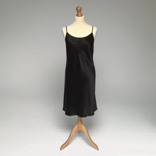 Load image into Gallery viewer, A black silk satin slip displayed on a cream mannequin torso with a wooden stand against a light gray studio background.

