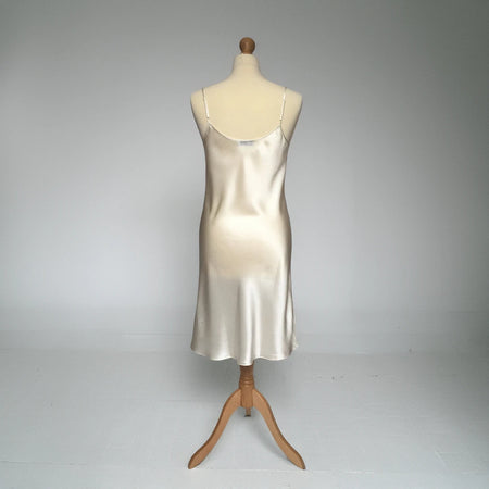 A silk satin slip dress in ivory color, displayed on a mannequin against a neutral gray studio background.