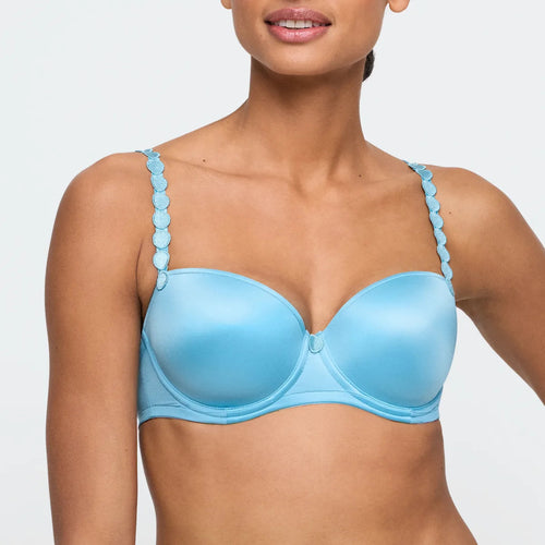 Woman wearing a blue bra with decorative straps on a light gray background