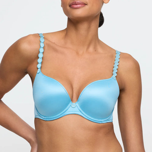 Woman wearing a light blue bra with decorative straps on a plain background
