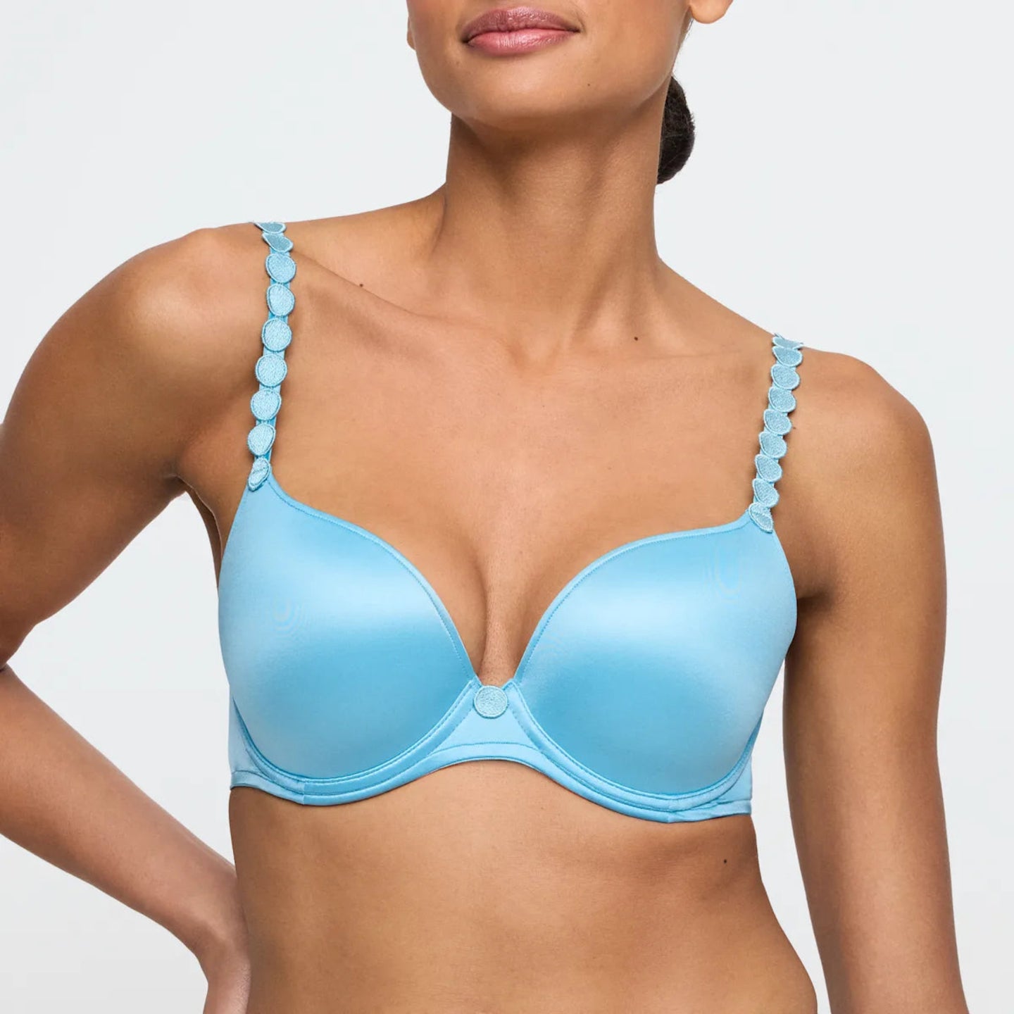 Woman wearing a light blue bra with decorative straps on a plain background